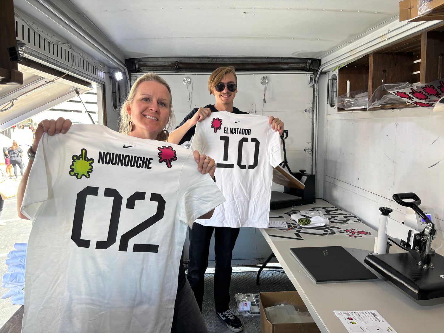 Two event printers holding up shirts with customized names that were just printed live on heat presses at a Nike Soccer event in Nashville, Tennessee.