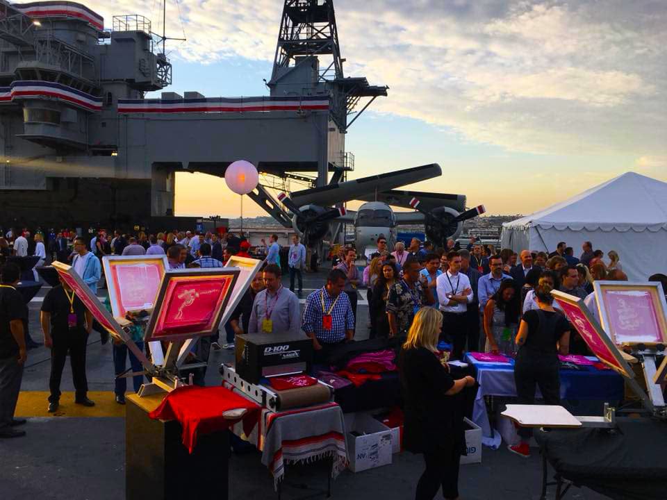 A live screen printing event for a fortune 500 company on the USS Midway in San Diego, California with happy guests waiting to get their shirts.