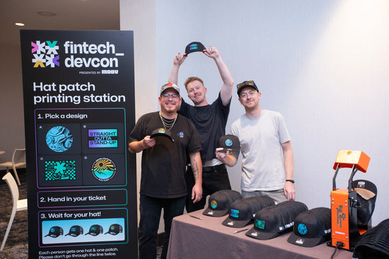 Three live printing technicians showing off freshly customized hats at a live hat bar at the Denver Convention Center at a Denver, premier Colorado tech conference.