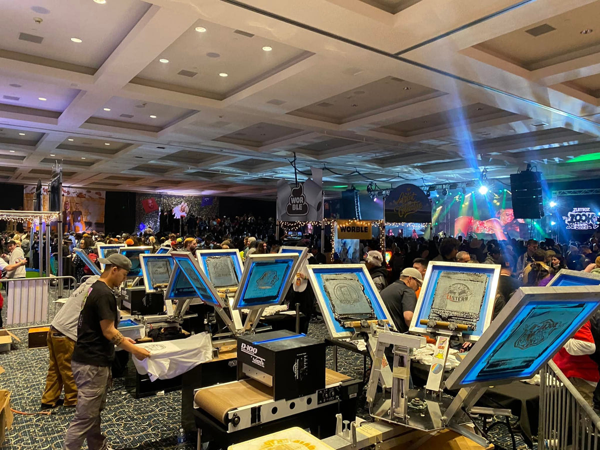 A large event hall with live screen printing technicians printing custom t-shirts on press machines at an event for Fortune 500 companies.