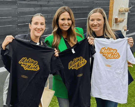 Three happy women holding freshly printed t-shirts at a live screen printing event in downtown San Diego.