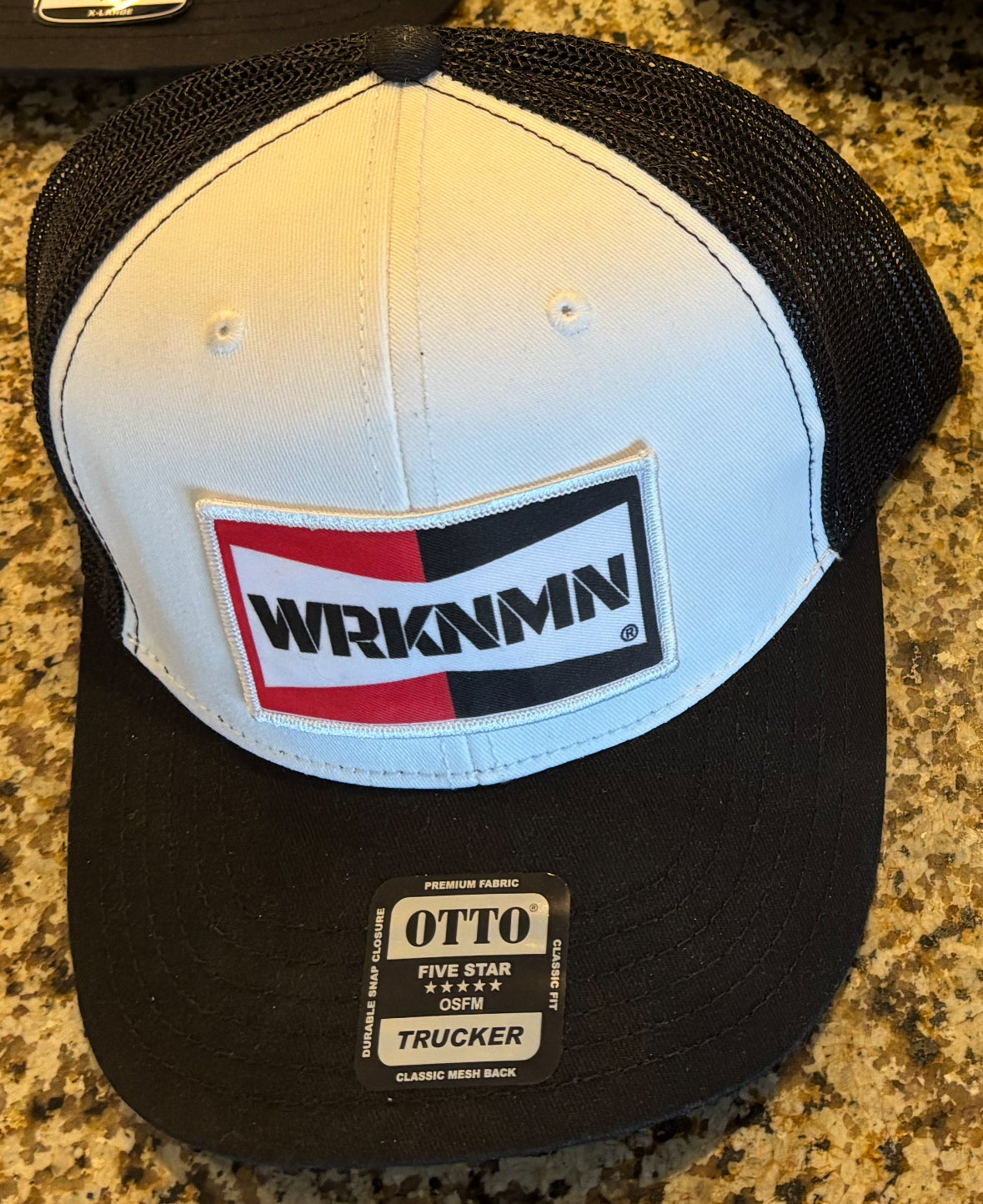 Black and white cap with WRKNMN logo on a granite surface
